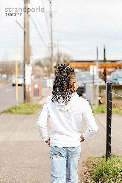 Junges Kind mit langen lockigen Haaren läuft den Bürgersteig der Stadt entlang