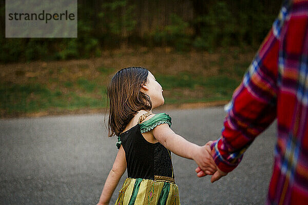 Ein kleines Kind im Prinzessinnenkostüm hält beim Spaziergang die Hände seines Vaters