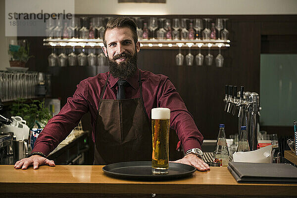 Porträt eines jungen Mannes an der Bartheke mit einem Glas Bier im Tablett