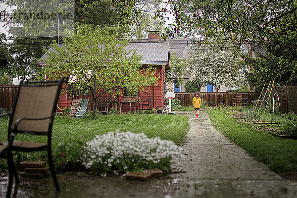 A small child stands in rain at end of long path in backyard