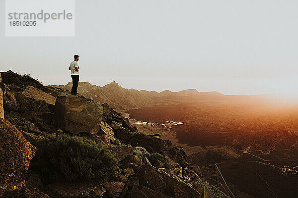 Ein Mann steht auf einem Berggipfel und beobachtet den Sonnenuntergang