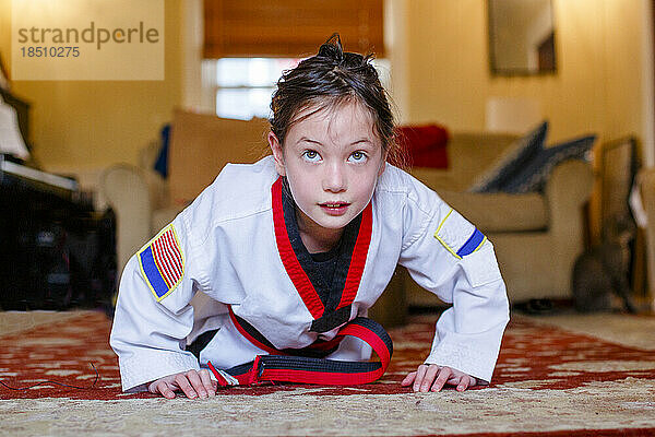 A fierce girl in Taekwondo uniform does pushups in living room