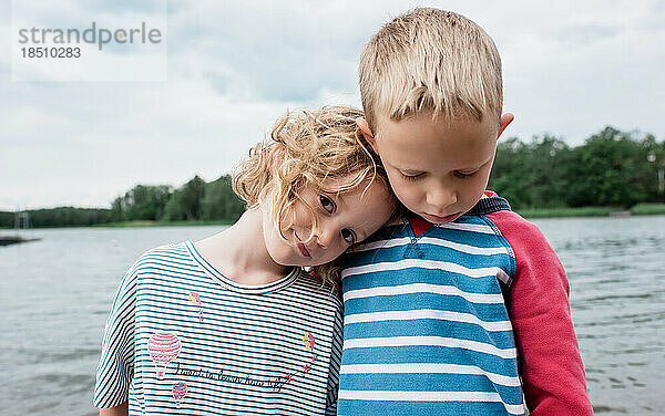 Porträt von Geschwistern  die sich im Sommer im Urlaub am Strand umarmen