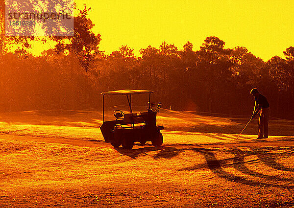 Silhouette eines Mannes und eines Golfwagens vor dem lebhaften Sonnenuntergang