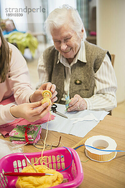 Ältere Frau mit Mädchen hält handgemachtes Häkelküken im Pflegeheim