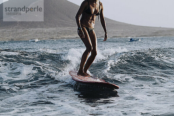 Unterer Teil einer Surferin im Bikini  die im Meer surft