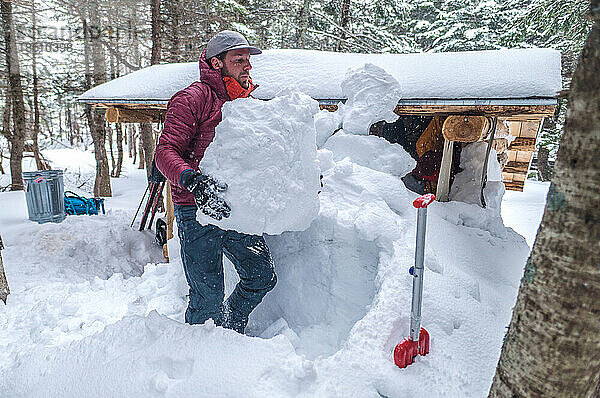 Mann schaufelt im Winter Schnee vor der Hütte