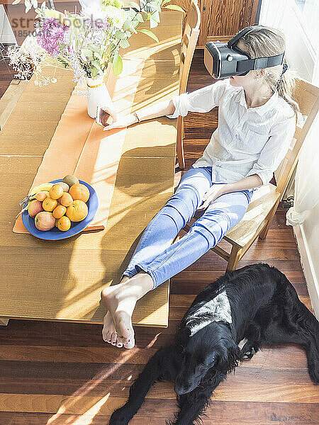 Mädchen mit Virtual-Reality-Brille im Wohnzimmer  Hund entspannt auf dem Boden