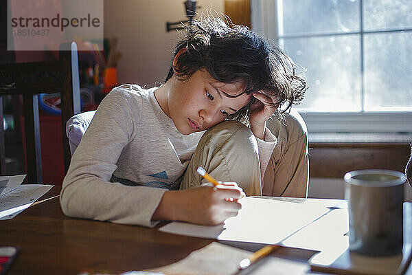 Ein Kind mit dem Kopf in den Händen konzentriert sich zu Hause auf Schulaufgaben