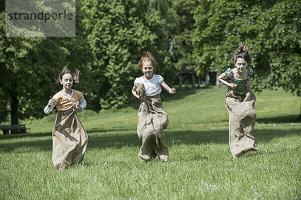 Drei Mädchen springen beim Sackhüpfen auf einem Feld  München  Bayern  Deutschland