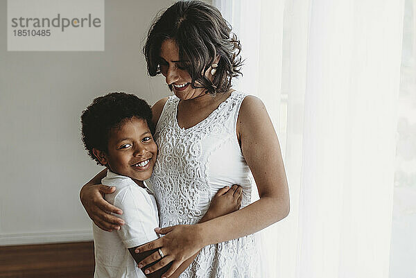 Mittlere Ansicht eines lächelnden Sohnes  der von einer lächelnden Mutter im Studio umarmt wird