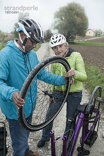 Älteres Paar stellt Fahrradrad auf unbefestigter Straße ein  Bayern  Deutschland