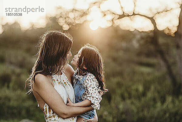 Seitenansicht von Mutter und Tochter  die sich im sonnigen Feld umarmen