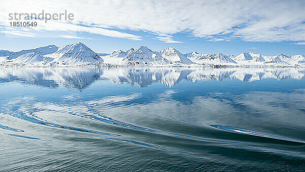 Schneebedeckte Berge spiegeln sich im Meer  im Vordergrund wacht ein Boot auf