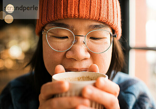 Nahaufnahme Porträt einer asiatischen Frau  die ihren Kaffee in einem Café hält