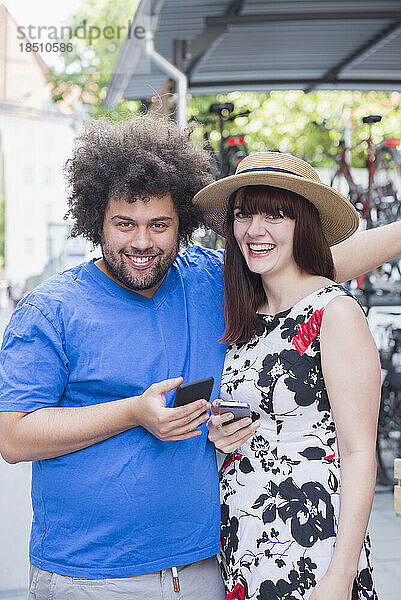 Porträt eines glücklichen Paares  das Mobiltelefone in der Stadt benutzt