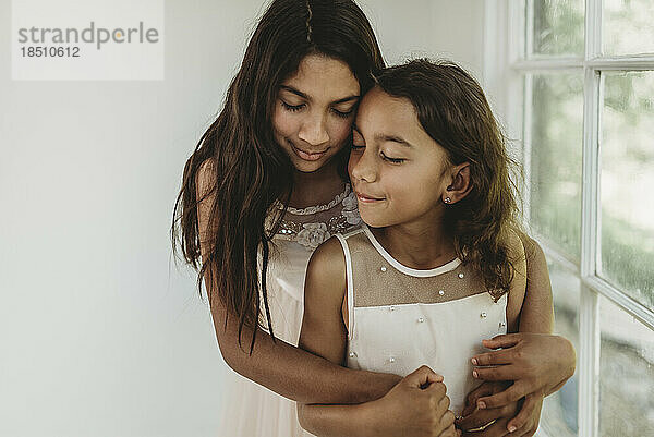 Sisters hugging in natural light studio while closing eyes