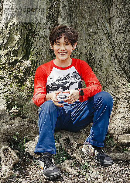 A smiling boy sits at base of oak tree