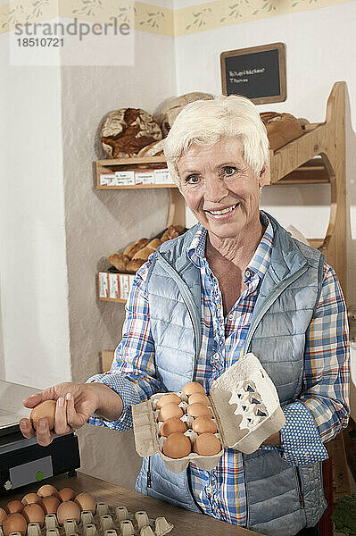 Porträt eines Verkäufers  der im Laden Eier in Eierkartons arrangiert und lächelt  Bayern  Deutschland
