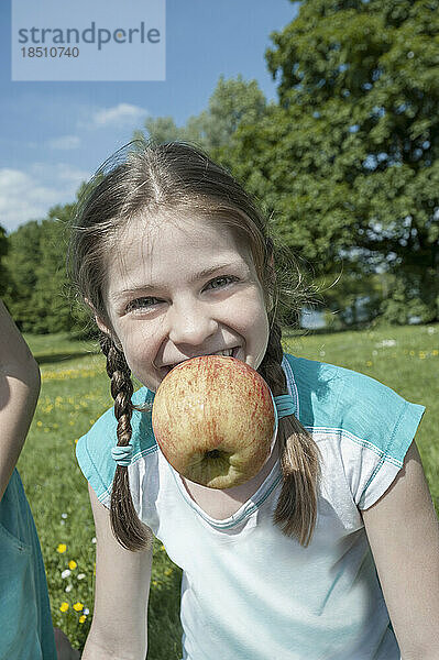 Porträt eines Mädchens mit Apfel im Mund und lächelnd  München  Bayern  Deutschland