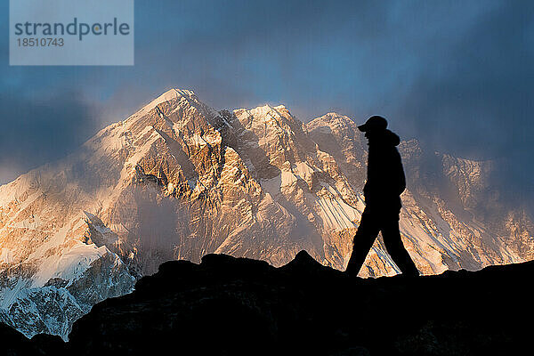 Ein Mann geht bei Sonnenuntergang in Silhouette auf einem Bergrücken mit Nuptse im Himalaya-Hintergrund.