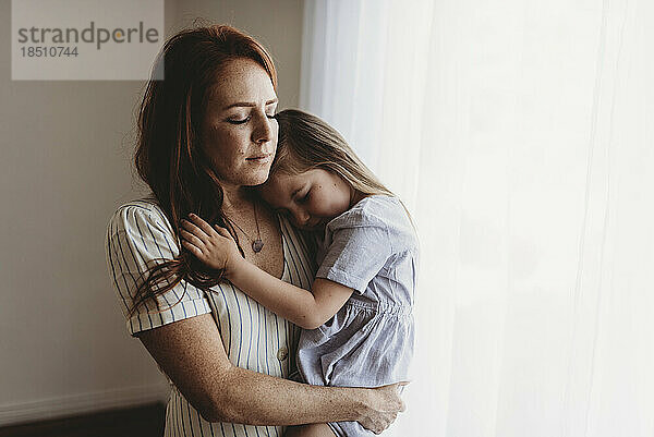 Junge Mutter kuschelt mit ihrer kleinen Tochter  während sie im Studio die Augen schließt