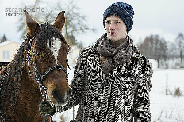 Junger Mann steht im Winter mit Pferd auf Ackerland  Bayern  Deutschland