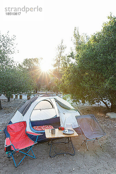 Leerer Campingplatz mit Zelt und Campingstühlen an einem sonnigen Tag im Freien.