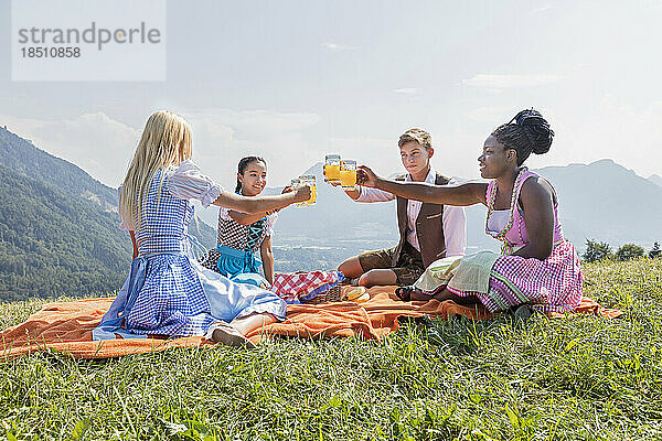 Teenager-Freunde klirren beim Picknick mit Gläsern Orangensaft  Bayern  Deutschland