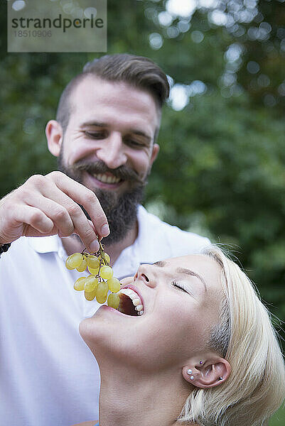 Junger Mann füttert seine Frau im Garten mit Weintrauben  Bayern  Deutschland