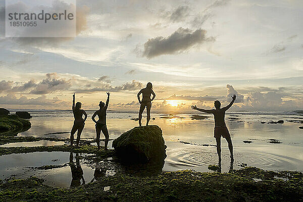 Silhouette von Freunden  die bei Sonnenuntergang über dem Meer ausgestreckt sind  Uluwatu  Bali  Indonesien