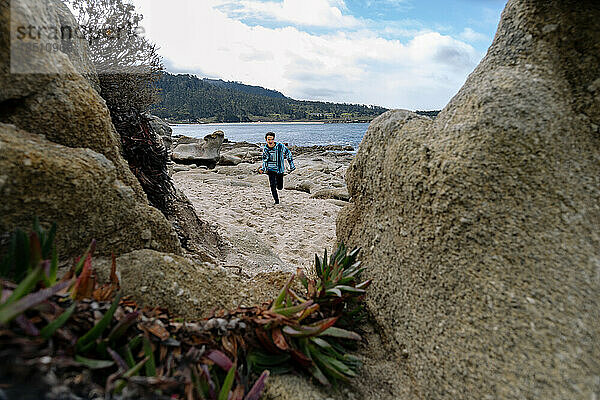 Junge  umrahmt von Felsen am Strand  rennt in Richtung Kamera