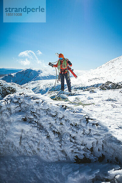 Skibergsteiger wickelt Seil mit schneebedeckten Bergen dahinter