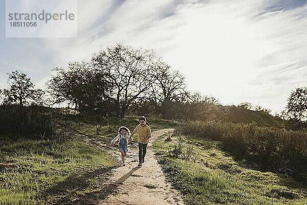 Bruder und Schwester halten sich an den Händen und laufen durch ein Feld mit Hintergrundbeleuchtung