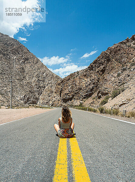 Ruhige Frau sitzt auf einer leeren Straße und blickt auf Berge