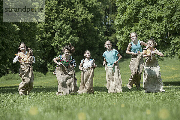 Eine Gruppe von Mädchen springt beim Sackhüpfen auf einem Feld  München  Bayern  Deutschland