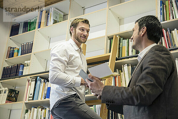 Zwei Männer schauen einander vor einem Bücherregal an  Bayern  Deutschland