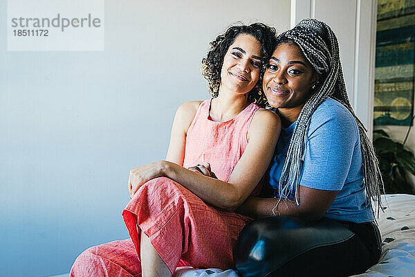 Porträt eines lächelnden lesbischen Paares  das zu Hause im Bett sitzt
