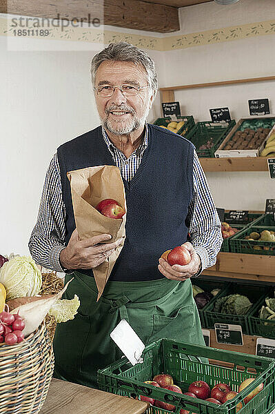 Porträt eines älteren Ladenbesitzers  der Äpfel im Laden verkauft  Bayern  Deutschland