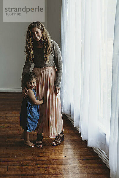 Full length portrait of mother and daughter smiling at camera in studi