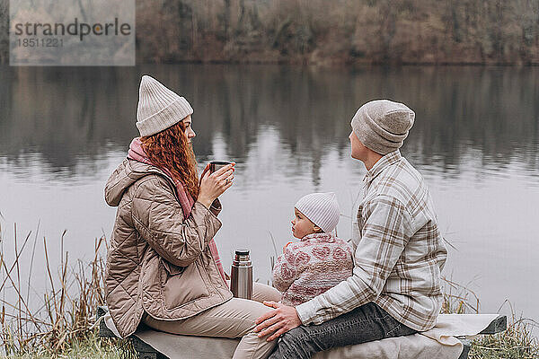Eltern und ein kleines Mädchen entspannen sich in einem Frühlingspark in der Nähe des Flusses