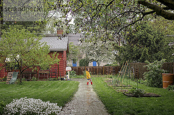 Fernsicht auf ein Kind  das im Regen in Stiefeln im Hinterhof spielt