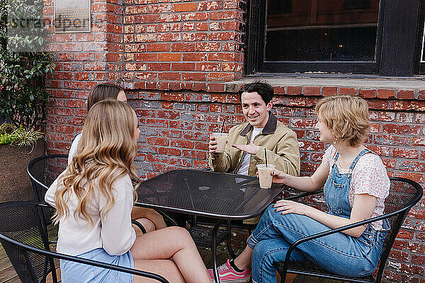 Eine Gruppe von Freunden unterhält sich fröhlich am Tisch draußen in der Innenstadt