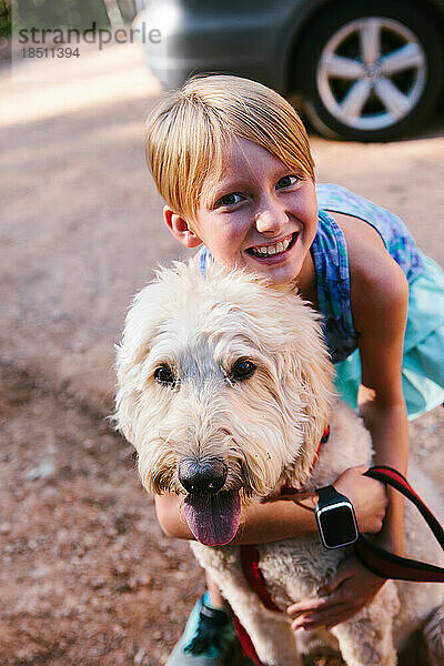 Das Kind umarmt im Sommer glücklich seinen weißgoldenen Doodle-Hund