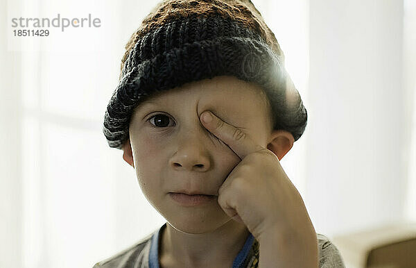 Porträt eines kleinen Jungen  der mit einem Auge in die Kamera schaut und einen Hut trägt