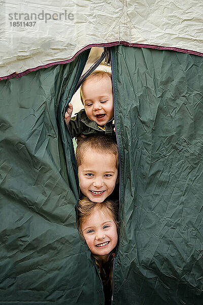Drei lächelnde Kinder schauen aus dem Campingzelt