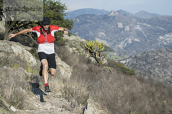 Ein agiler Mann mittleren Alters springt beim Trailrunning in El Arenal  Hidalgo  Mexiko  über einen Felsen.