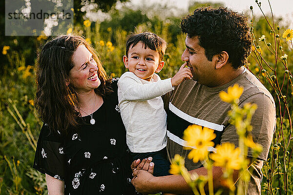 Latino-Vater und Mutter lachen mit ihrem kleinen Sohn im Blumenfeld