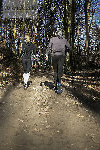 Rückansicht eines Mannes und einer Frau in Sportbekleidung beim Joggen auf einem Waldweg