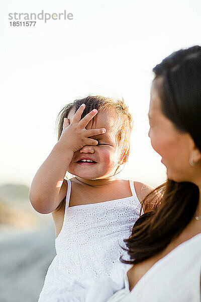 Mutter hält Kleinkind mit der Hand auf dem Gesicht am Coronado Beach in San Diego